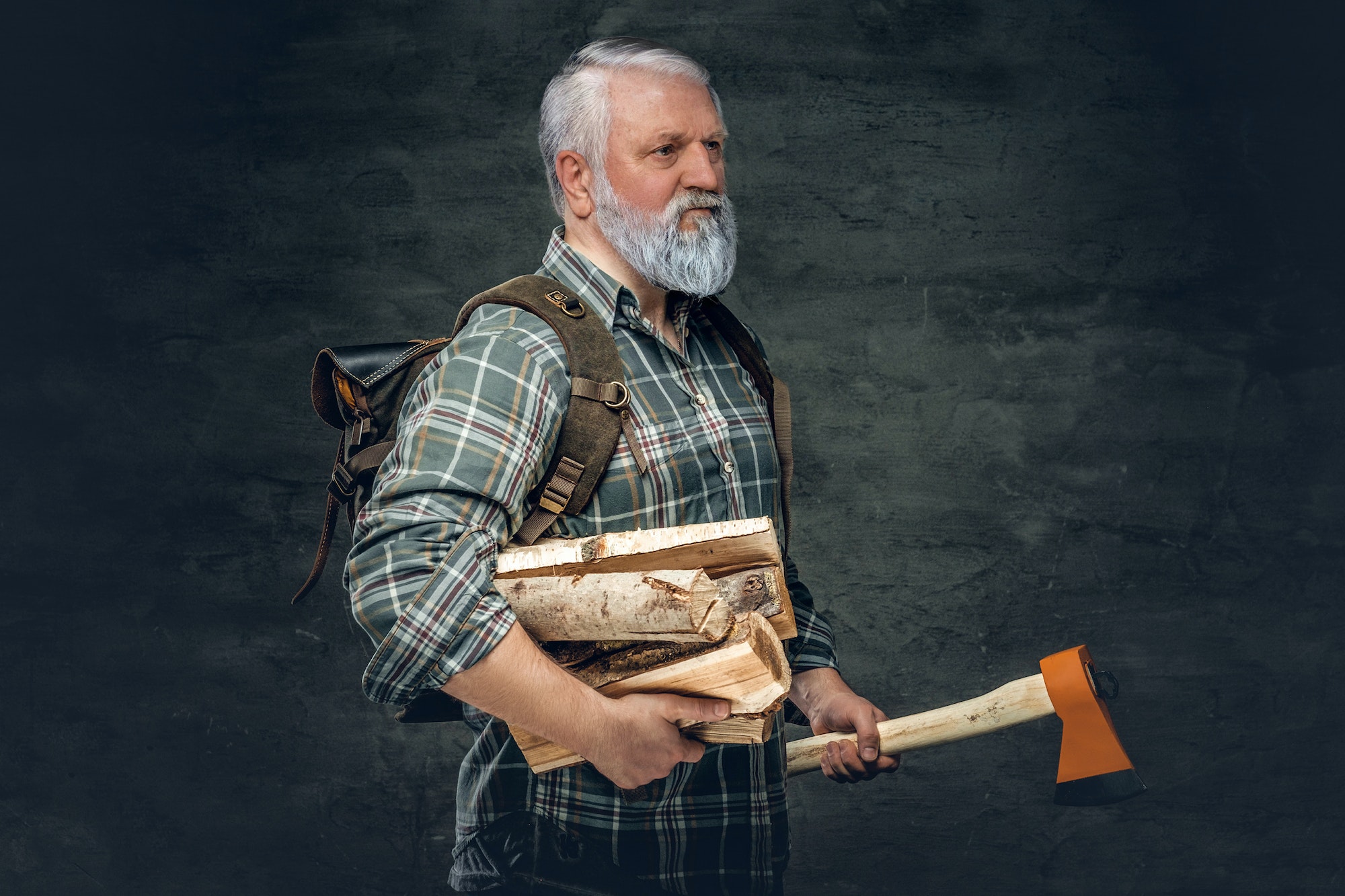 Old man woodcutter holding axe and firewood against dark background