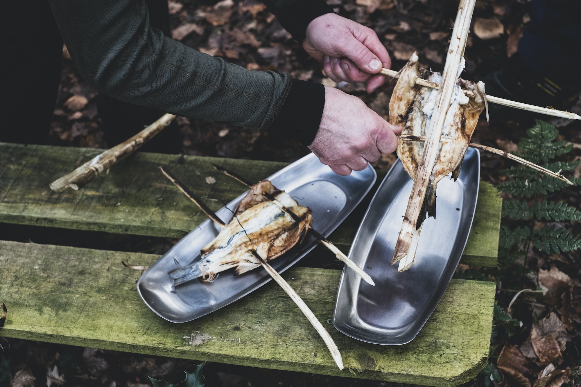 High angle close up of person placing grilled fish on wooden skewers on metal plates, cooking